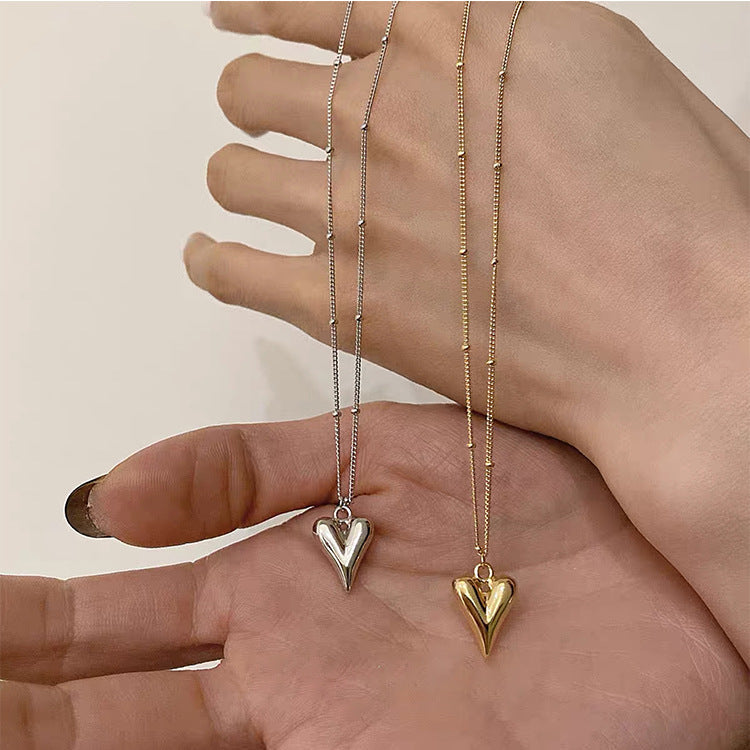 Comparison of the 3D heart pendant necklace in both silver and gold stainless steel finishes held in hand.