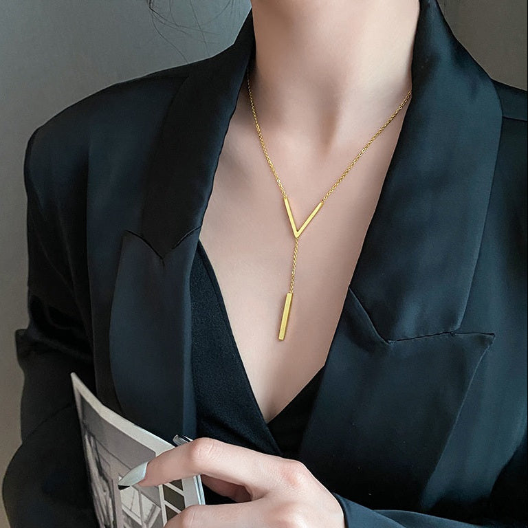Detailed view of the gold-plated lariat necklace on a model wearing a black suit jacket, highlighting the elegant drop of the vertical bar pendant.