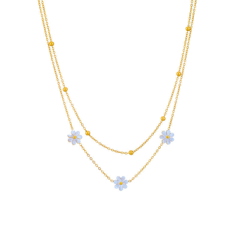 Studio shot of the 18K gold PVD plated double strand necklace with three white flower charms and gold bead accents.