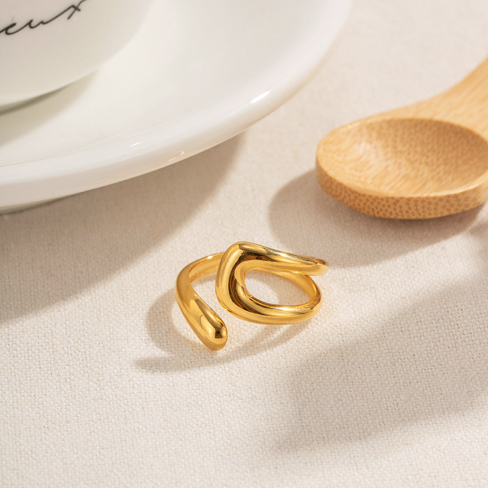 A gold-plated irregular statement ring displayed on a textured white surface next to a wooden spoon and white ceramic.