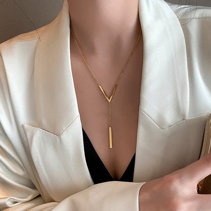 A model wearing the minimalist gold V and bar lariat necklace styled with a professional white blazer and a black V-neck top.