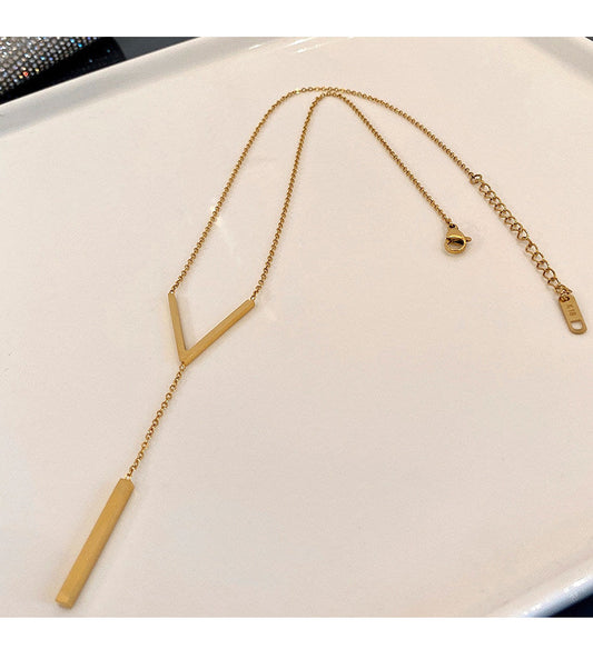 A top-down view of the 18K gold-plated stainless steel Y-necklace with its geometric V-bar pendant laid out on a clean white display surface.