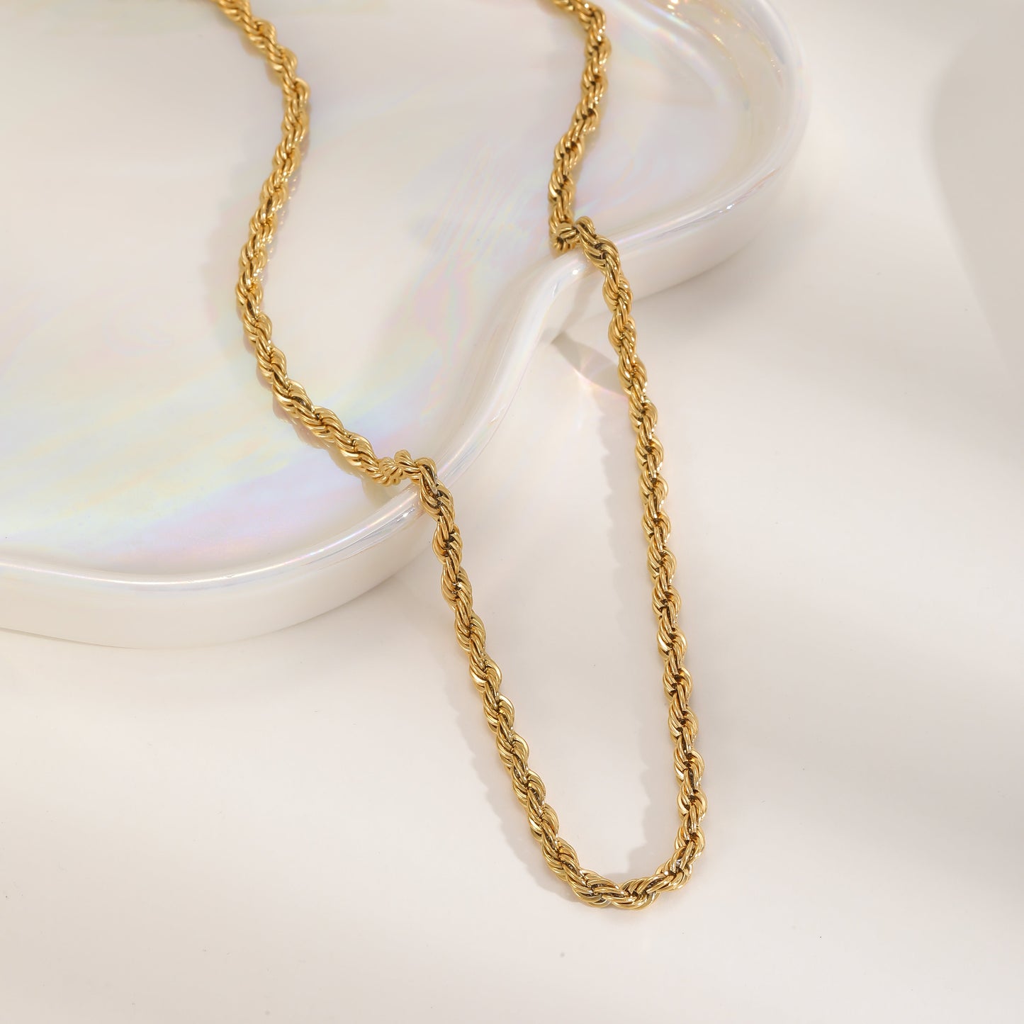 Aesthetic shot of a gold-plated 304 stainless steel rope chain draped over a white iridescent decorative heart-shaped tray.