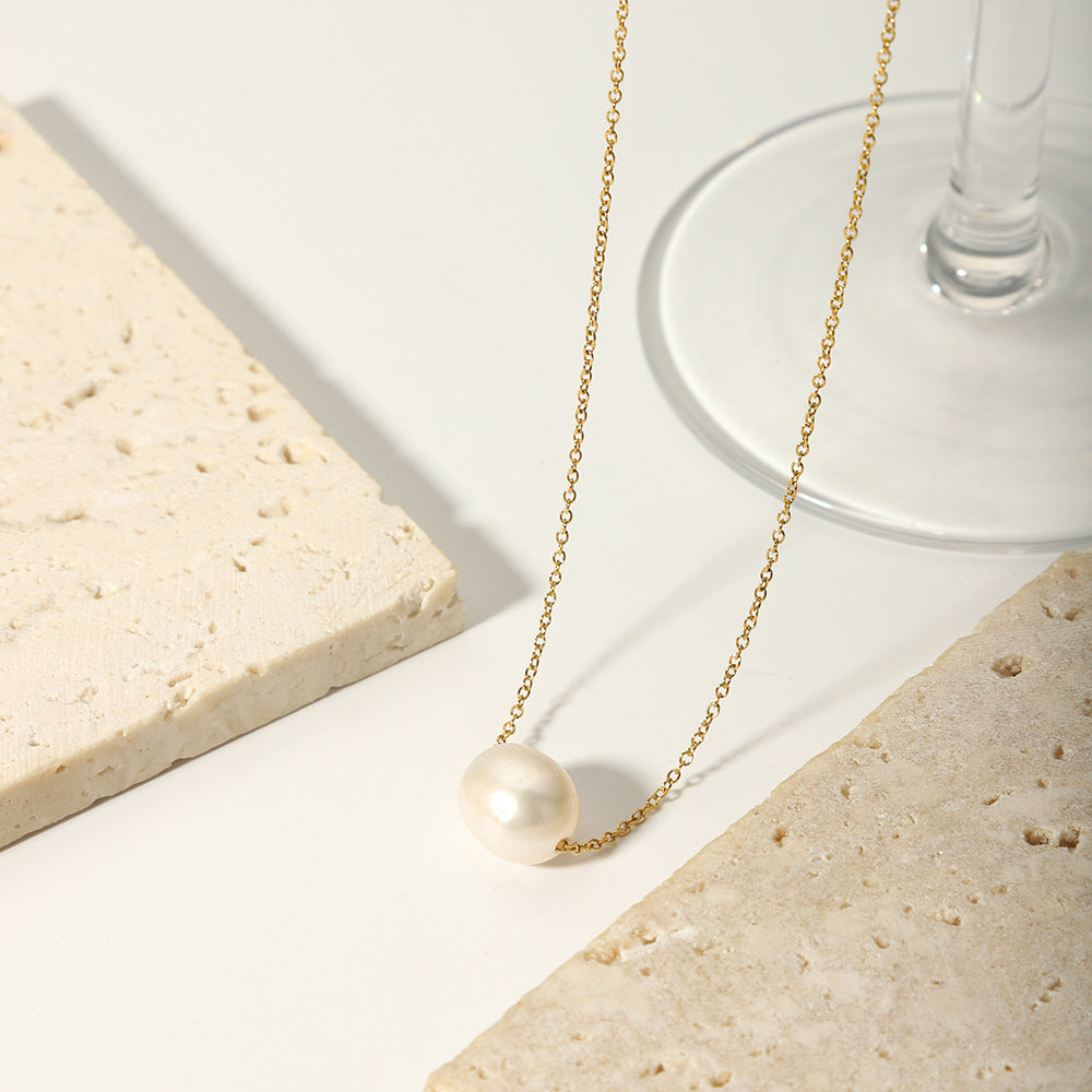 Aesthetic shot of the floating pearl necklace draped over a white stone base near a clear glass.