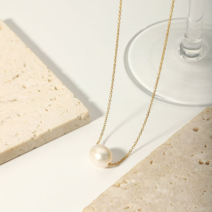 Aesthetic shot of the floating pearl necklace draped over a white stone base near a clear glass.