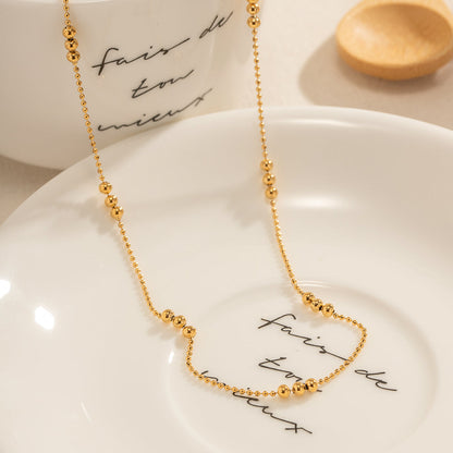 Aesthetic shot of the gold ball chain sitting on a white ceramic plate with French text.