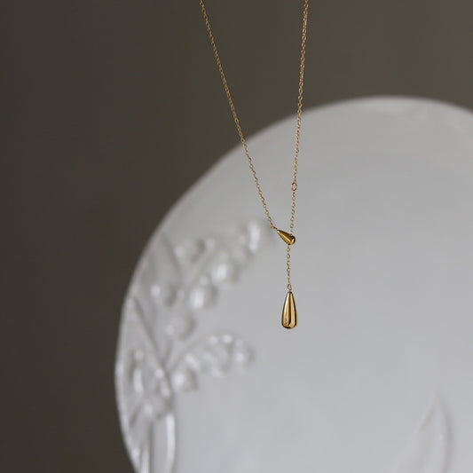 Aesthetic shot of the gold teardrop Y-necklace displayed against a white decorative ceramic plate.