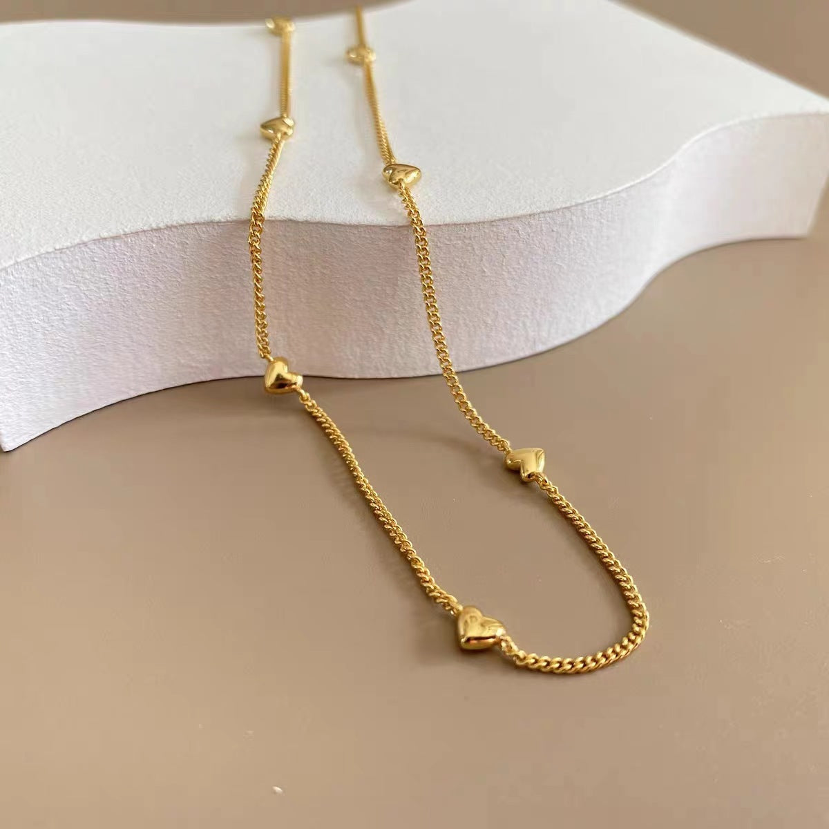 Aesthetic shot of the multi-heart gold necklace draped over a white curved platform.