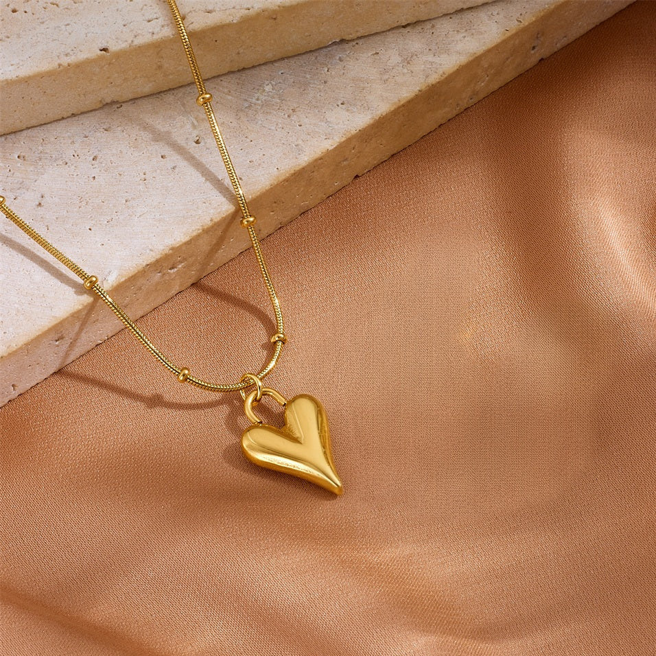 Close-up of a 18K gold plated 3D puffy heart pendant on a satellite bead chain resting on a silk background.