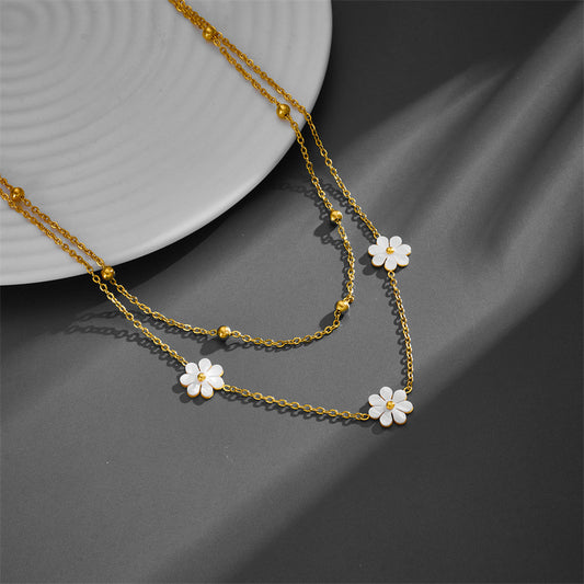 Close-up of a double-layer gold cable chain necklace featuring white acrylic daisies on a textured gray background.