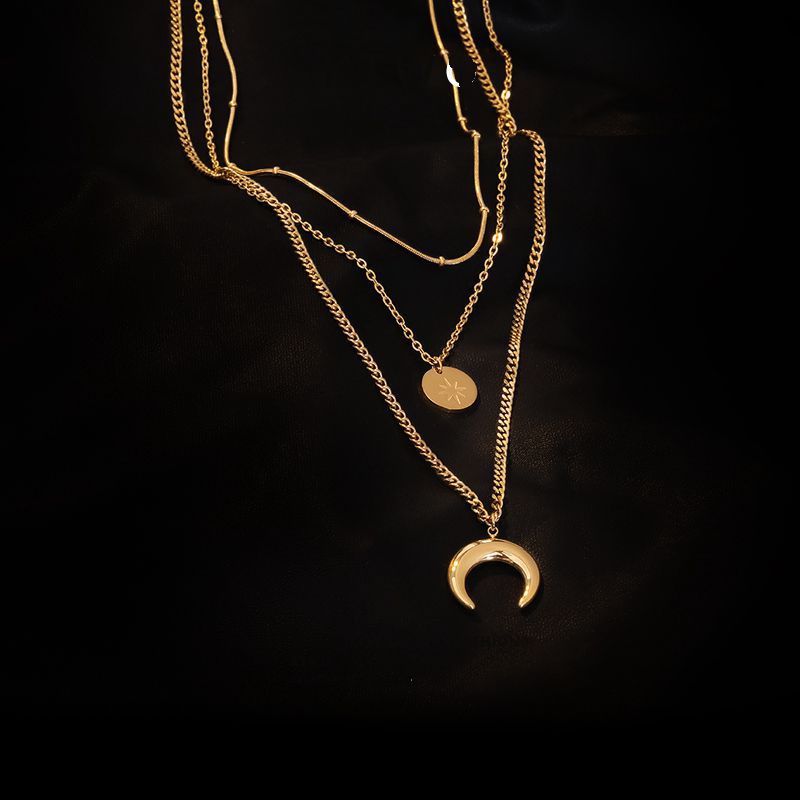 Close-up of a gold-plated triple strand necklace on a dark background showing snake, cable, and curb chain details.