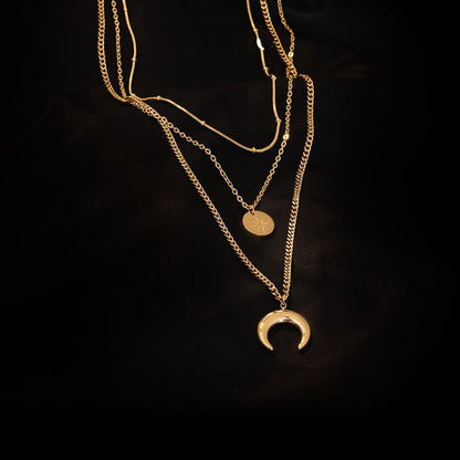 Close-up of a gold-plated triple strand necklace on a dark background showing snake, cable, and curb chain details.