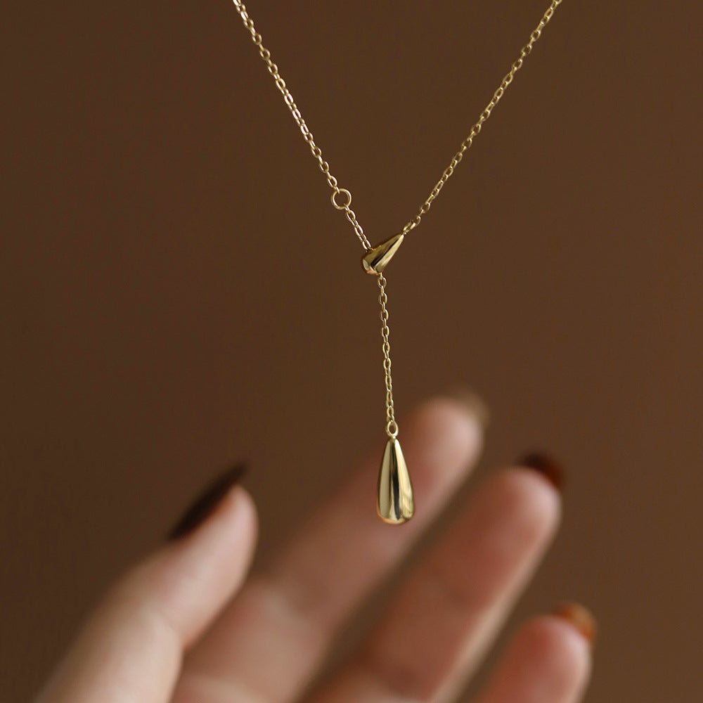 Close-up of a hand holding a minimalist gold lariat necklace featuring a polished water droplet pendant.