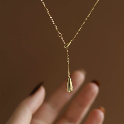 Close-up of a hand holding a minimalist gold lariat necklace featuring a polished water droplet pendant.