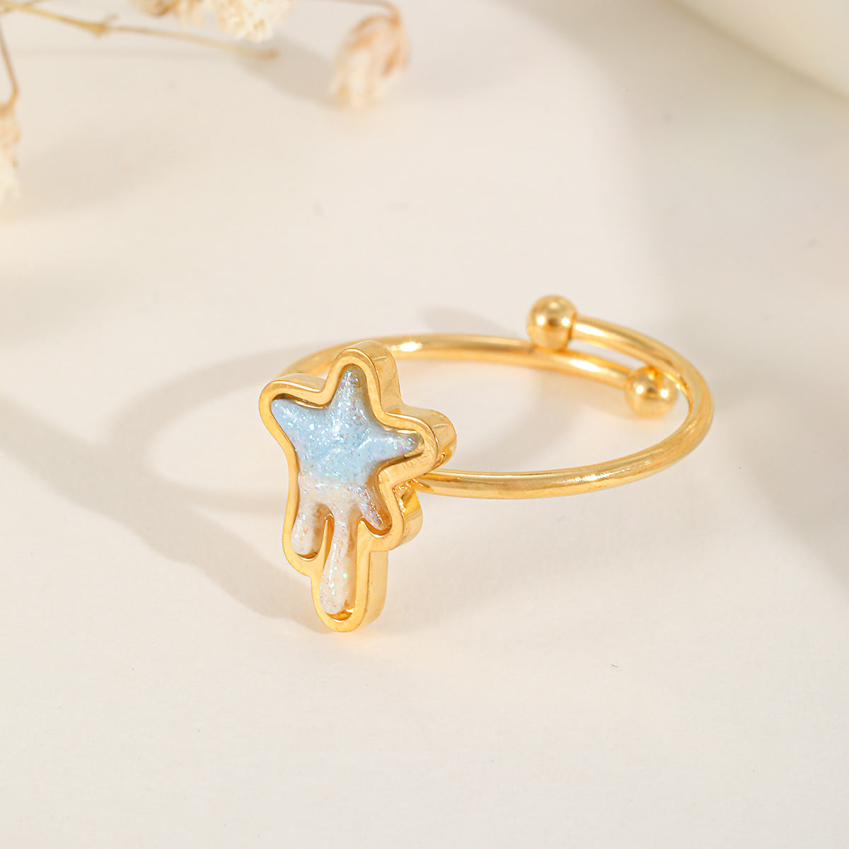 Close-up of an adjustable gold ring featuring a celestial star motif with light blue shimmering resin inlay.
