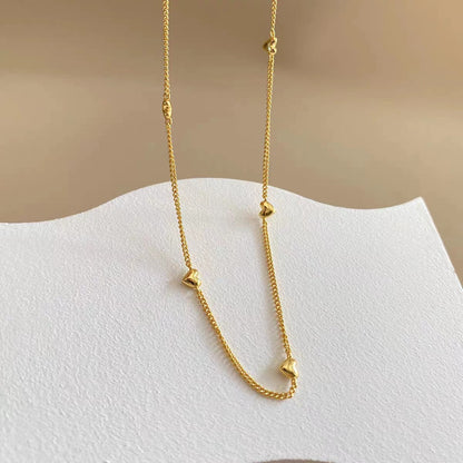Close-up of the 18K gold plated heart station necklace showing the small heart charms along the delicate chain.