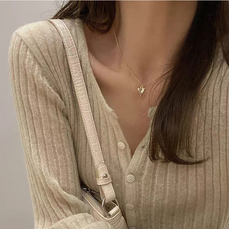 Close-up view of the gold heart pendant sitting elegantly on a model's neckline against a neutral knit sweater.