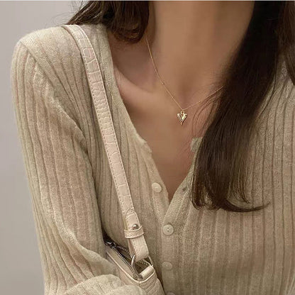 Close-up view of the gold heart pendant sitting elegantly on a model's neckline against a neutral knit sweater.