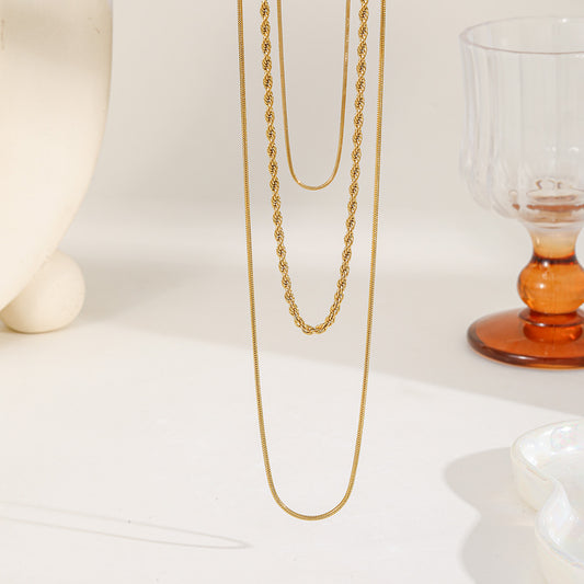 Close up of a three-layer gold necklace set featuring two thin snake chains and one twisted rope chain on a white minimalist background