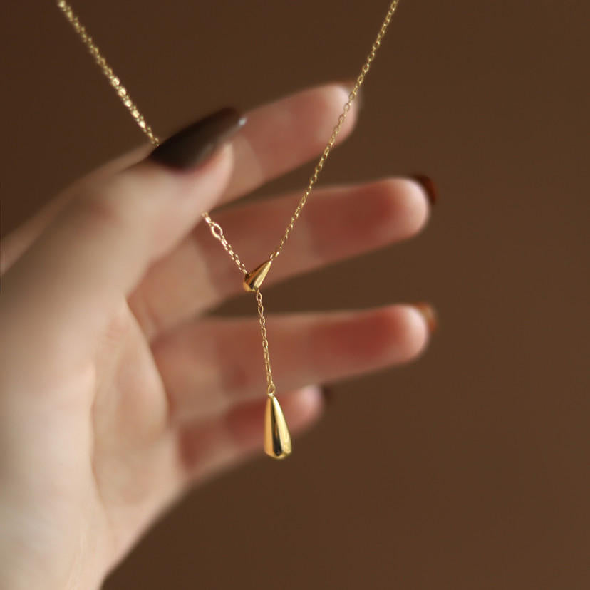 Detailed view of the 18K gold plated cable chain and water droplet charms held against a brown background.