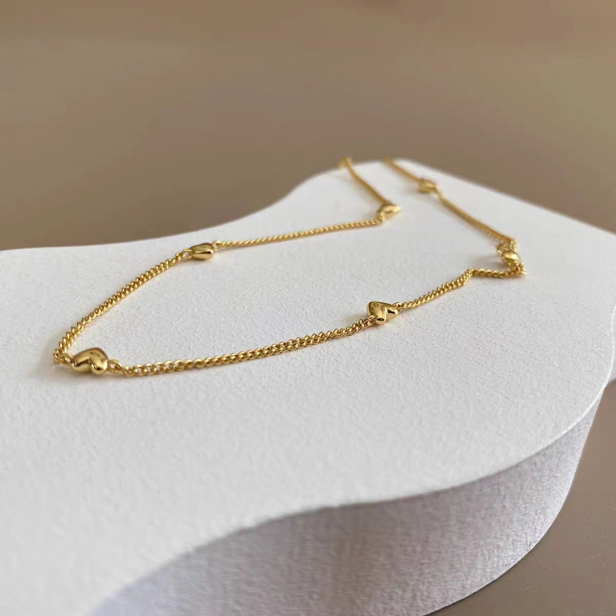 Flat lay view of the waterproof 18K gold station necklace on a minimalist surface.