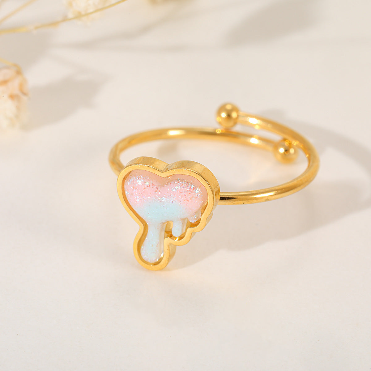Detailed shot of a gold adjustable ring featuring a unique "dripping" heart charm with pink and blue iridescent resin.