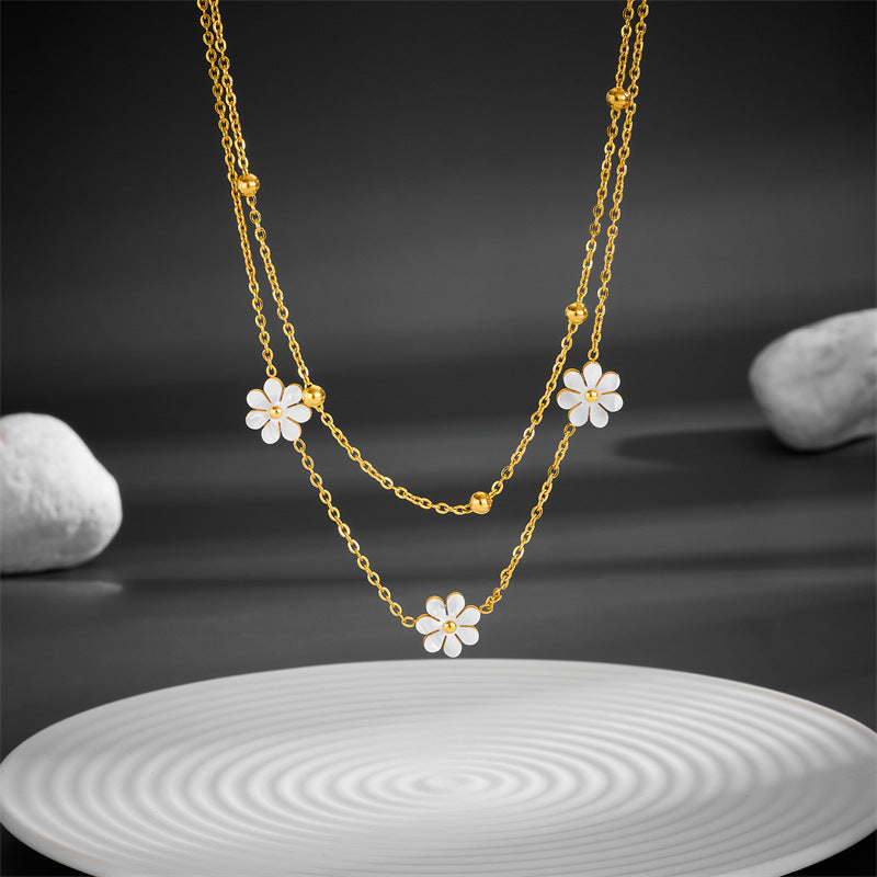 High-angle view of the layered gold chain with white flower pendants hanging over a white ripple-textured plate.