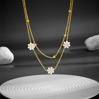 High-angle view of the layered gold chain with white flower pendants hanging over a white ripple-textured plate.