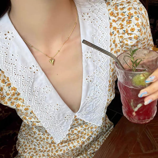 Lifestyle shot of a model wearing the gold heart necklace with a floral V-neck dress, showcasing its daily wear appeal.