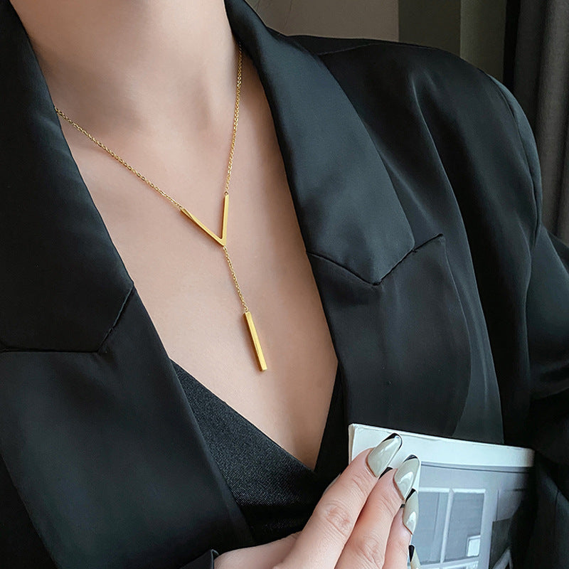 Lifestyle shot of the gold Y-necklace on a model, showing the delicate cable chain and geometric pendant as a "Commute" style accessory.
