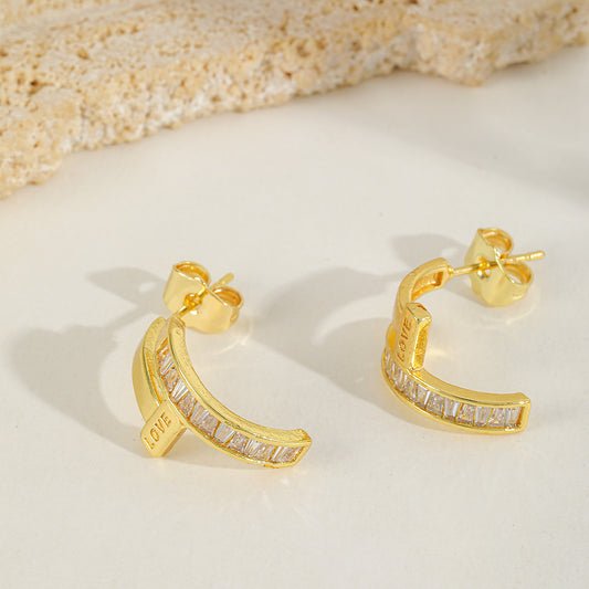 Close-up of a pair of curved gold ear studs featuring vertical zircon inlays and the word "LOVE" engraved on the side.