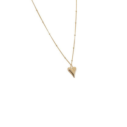 Minimalist studio shot of the gold heart pendant necklace on a clean white background, highlighting the satellite chain.