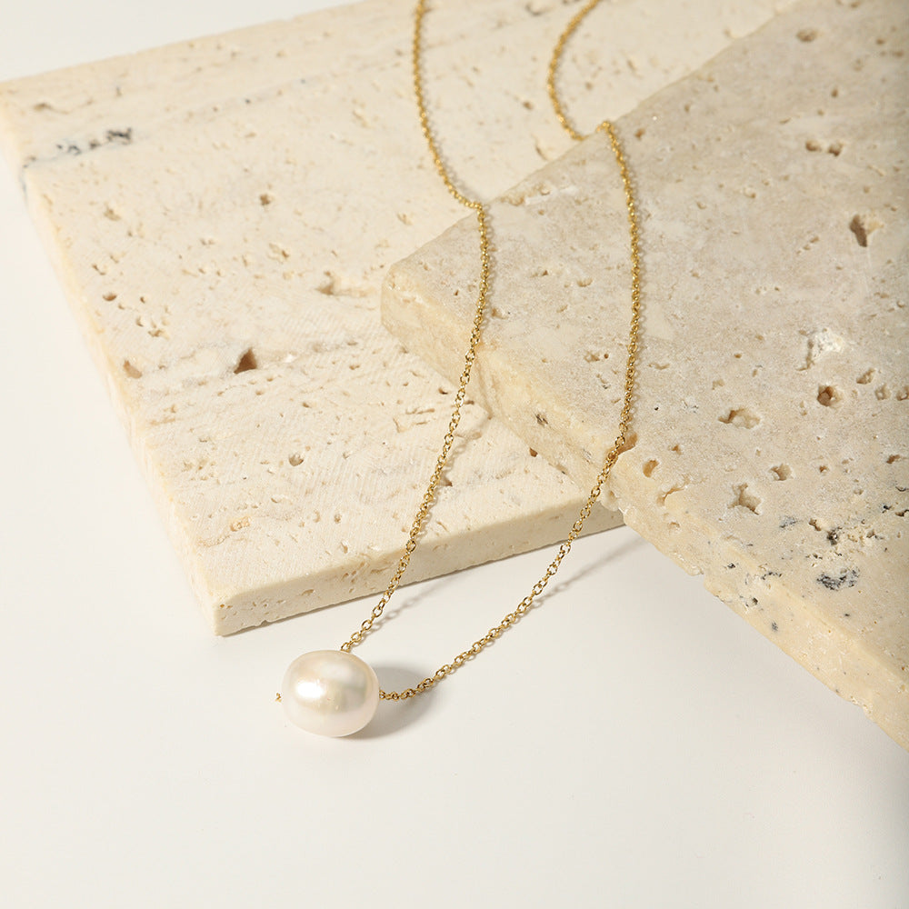 The gold-plated stainless steel pearl necklace laid out on stacked neutral-toned stones.