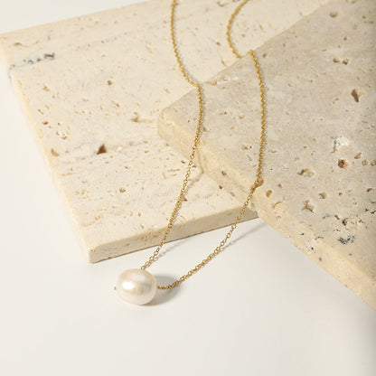The gold-plated stainless steel pearl necklace laid out on stacked neutral-toned stones.