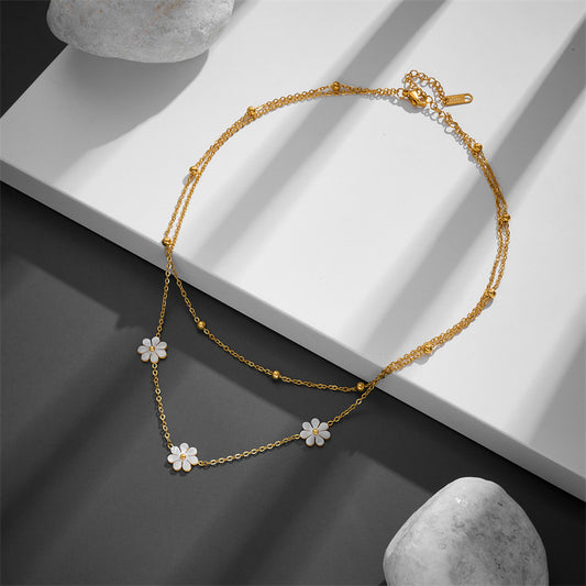 Top-down view of the layered daisy necklace displayed on a white and gray minimalist platform, showing the adjustable lobster clasp.